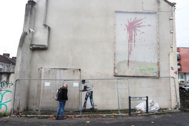 The artwork shows the man attempting to remove the wooden display which covers a Banksy artwork of a small child catapulting roses into the air
