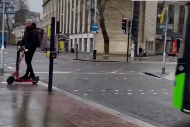 In the beginning of the video, an e-scooter rider zooms across a pedestrian crossing without looking and is seconds away from getting hit by a double-decker bus.