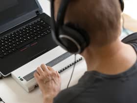 Global Accessibility Awareness Day focuses on digital access and inclusion for people with disabilities or impairments. (Image shows visually impaired person working on computer with assistive technology) 