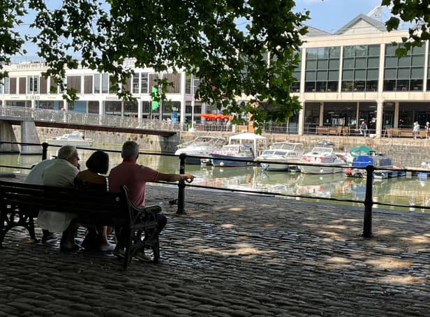 <p>A group of people sit in the shade as the sun basks down on the harbourside in Bristol</p>
