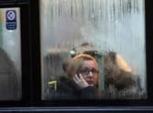 A woman looks out of the window of a bus as it waits at a bus stop in the rain in Bristol. 